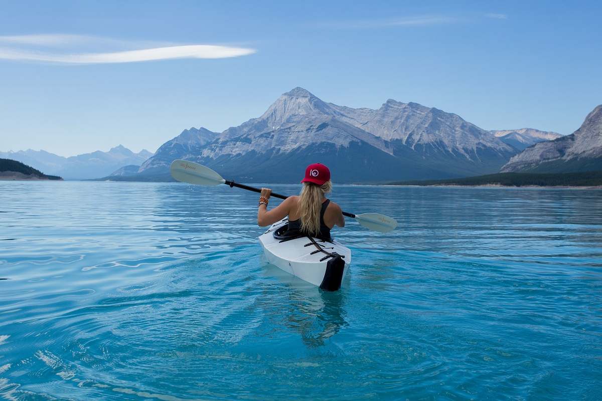 Kayakiste en pagaie simple sur lac bleu avec montagne enneigée au loin Kayakiste en pagaie simple sur lac bleu avec montagne enneigée au loin