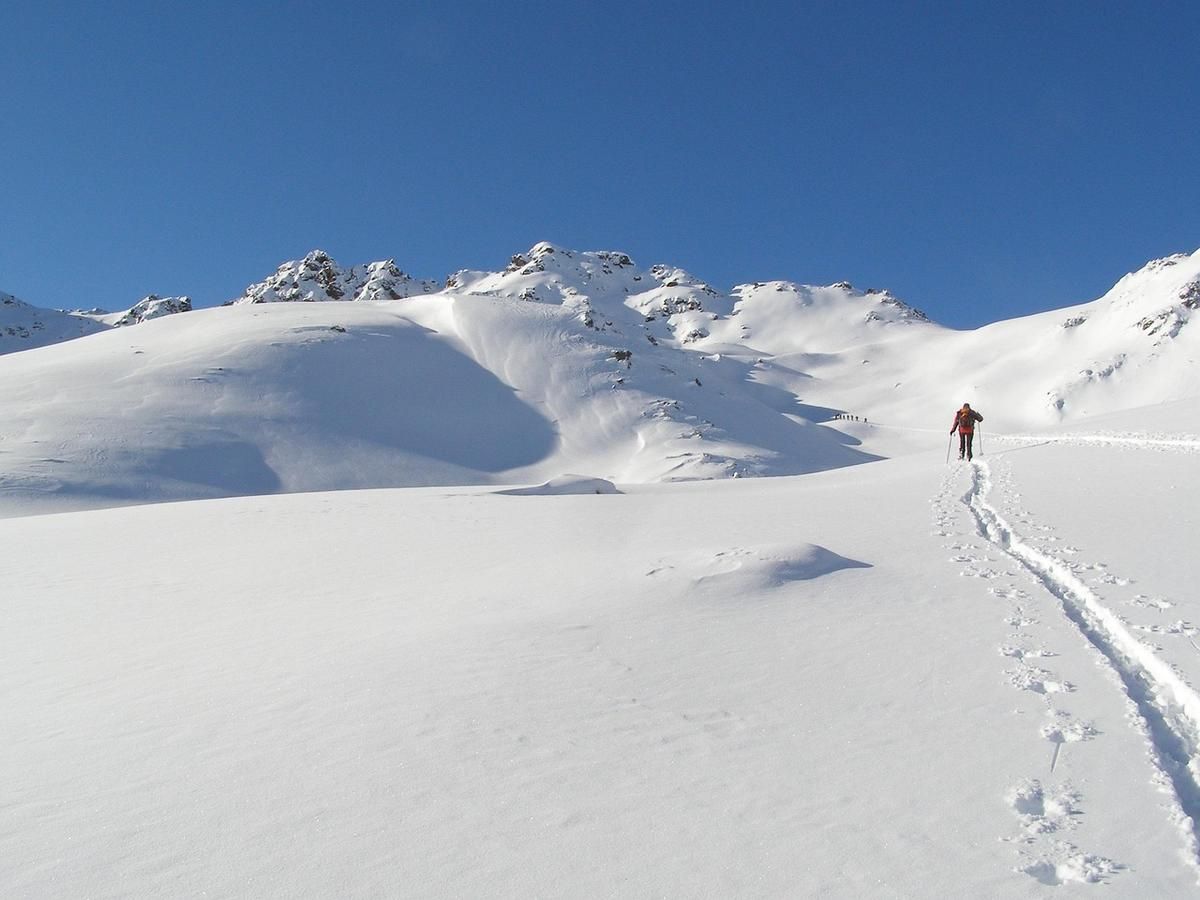 Personne marchant dans un champ enneigé avec des montagnes et un ciel bleu