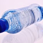 Une bouteille d'eau en plastique bleue avec son cap reflétée sur un fond blanc