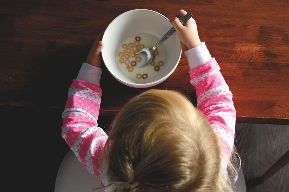 Une petite fille en pyjama rose mange des céréales au petit déjeuner